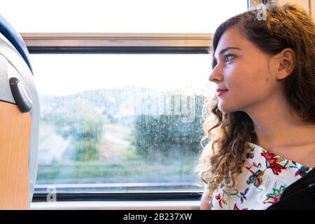 Woman young girl tourist sitting inside train in Italy with modern on seat side profile portrait closeup with view of Tuscany Stock Photo