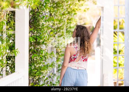 Young adult woman girl person in summer on sunny day in garden vine plant flowers outside gardening and wearing pastel fashion Stock Photo