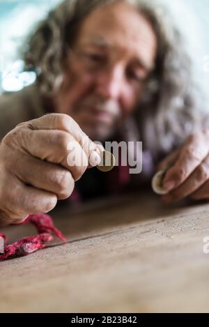 Conceptual image of poverty and personal crisis - senior man in torn sweater counting Euro coins. Stock Photo