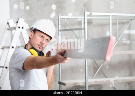 man work,  checks the straightedge to level the wall, with ladder and scaffolding in the interior construction site on background Stock Photo