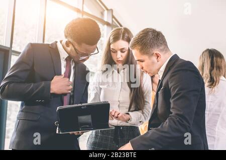 Business people in office having conversation and using digital tablet. Cheerful young African American man and Caucasian man and woman having busines Stock Photo