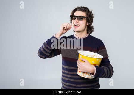 Young handsome man with beard over isolated white background with 3d glasses and holding a big bucket of popcorns while pointing front Stock Photo