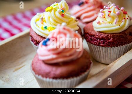 Red velvet cup cakes with white and rose topping from a fresh butter cream. Together with small colourful sprinkles like an anchor or also pineapple. Stock Photo