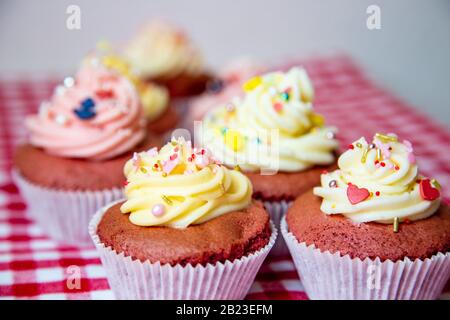 Red velvet cup cakes with white and rose topping from a fresh butter cream. Together with small colourful sprinkles like an anchor or also pineapple. Stock Photo