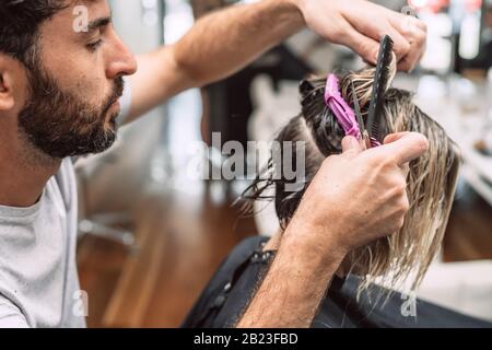 Master hairdresser cuts hair of blond woman in salon. Close up photo. Stock Photo