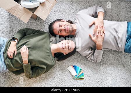 Overview of contemporary cheerful young couple in casualwear lying on the floor in their new house or flat Stock Photo