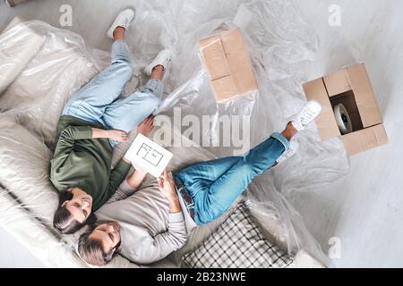 Overview of young restful couple in casualwear sitting on couch while discussing plan of their new flat or house Stock Photo