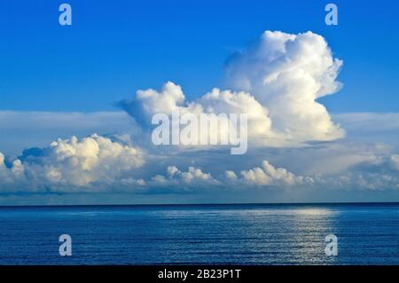 Cumulo Nimbus clouds on the horizon, lit from the side and reflected in the sea. Stock Photo