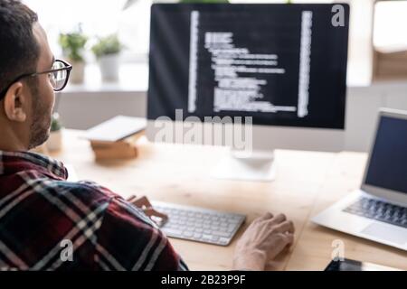 Part of young male software developer sitting by table in front of computer monitor while working with decoded data on screen Stock Photo