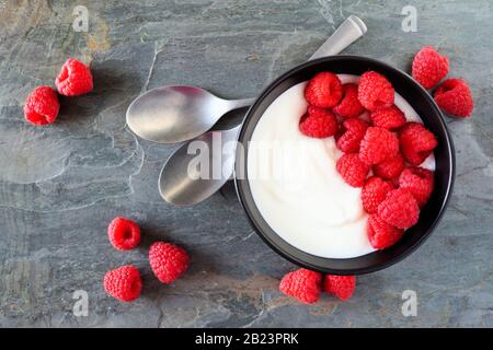 Bowl of yogurt with raspberries. Top view, table scene on a dark slate background. Stock Photo