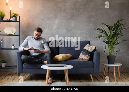 Young man in glasses angry talking on the phone sitting on the couch. Young businessman. Stock Photo