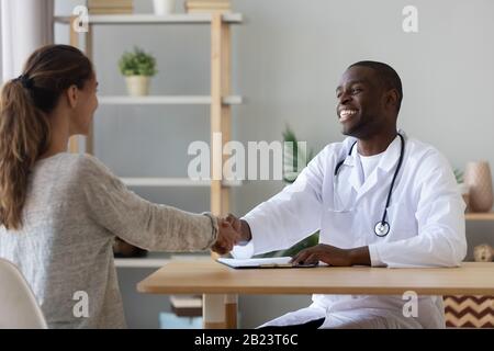 Smiling African American doctor shaking hand of female patient Stock Photo