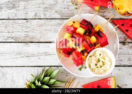 Grilled watermelon and pineapple fruit skewers with feta. Above view on a white wood table. Summer food concept. Stock Photo