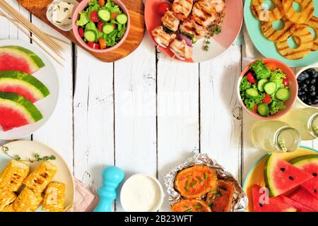 Summer BBQ or picnic food frame. Selection of grilled meat, fruits, salad and potatoes. Top view over a white wood background. Copy space. Stock Photo
