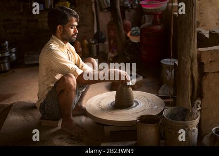 Traditional village potter at work using clay on turning wheel sitting on floor near Bundi, Rajasthan, India. Stock Photo