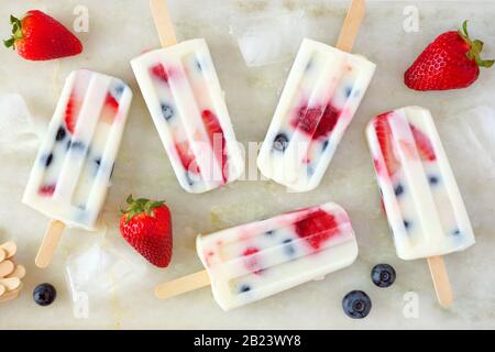 Healthy strawberry blueberry summer yogurt popsicles, top view scattered on a white marble background Stock Photo