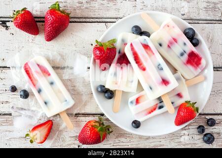 Healthy strawberry blueberry yogurt popsicles on a plate, above view summer table scene against a white wood background Stock Photo