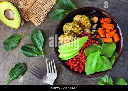 Healthy vegan buddha bowl with falafels, beet quinoa, avocado, and vegetables on a dark stone background. Healthy eating concept. Overhead scene.