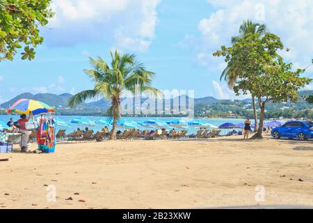 Castries, Saint Lucia - November 23, 2019. Tourists at Vigie Beach on a bright summer day, some under the shade of a FLOW sponsored umbrella Stock Photo