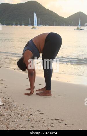 African lady with natural hair exercising stretching on the beach wearing a sports bra and black tights burning belly fat and staying fit and healthy Stock Photo