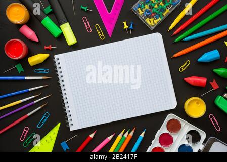 Empty checkered note pad surrounded by multicolored school supplies as fan isolated on black background, with copy-space Stock Photo