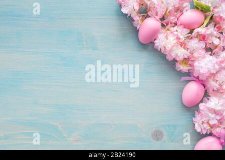 Spring Easter background of painted blue board with branch of flowering cherry covered with pink flowers and pink eggs as a border Stock Photo