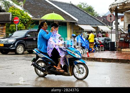 Two women with an umbrella riding a motor-bike in the rain, Luang Prabang, Laos Stock Photo