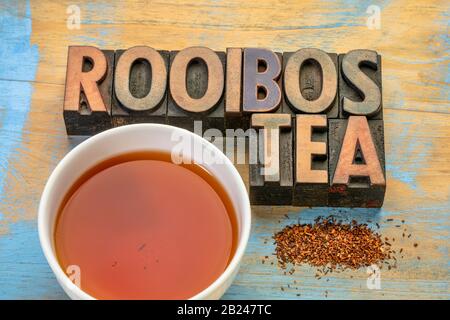 rooibos red tea  -  a white cup of a hot drink, loose leaves and typography in letterpress wood type on grunge wood background, tea made from the Sout Stock Photo