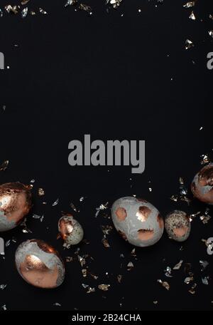 Gilded eggs and shiny confetti on a black background. Stock Photo