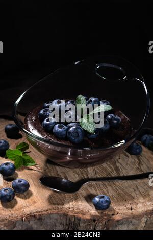 Chocolate pudding with blueberries, nicely arranged in a glass bowl on a wooden plate Stock Photo