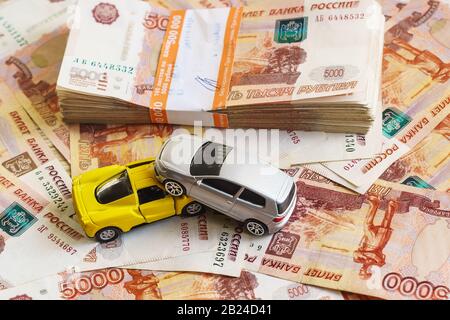 The concept of receipt of insurance premium after car accident: two toy cars and a stack of Russian rubles in the banking package lying on the backgro Stock Photo