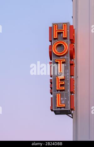 Neon hotel sign on the building corner against the sunset sky Stock Photo