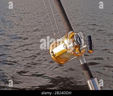a gold coloured Big Game 50 wide fishing reel closeup in used condition.  Located in a rod holder aboard a yacht, ready to deploy Stock Photo - Alamy