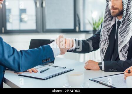 cropped view of multiethnic businessmen shaking hands and having deal on meeting Stock Photo