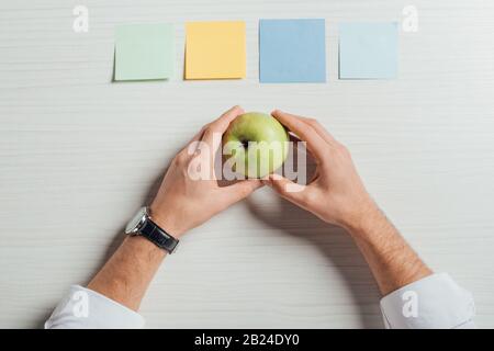 cropped view of businessman holding apple on table with empty note stickers Stock Photo