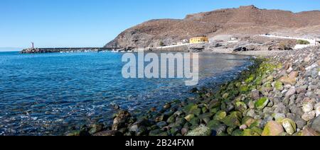 Panoramic view of Puerto de la Aldea with its pebble beach with moss in the foreground, on the island of Gran Canaria, Spain. Travel concept Stock Photo