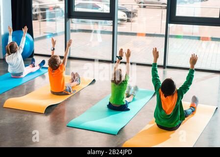 Back view of children with hands in air working out on fitness mats in gym Stock Photo