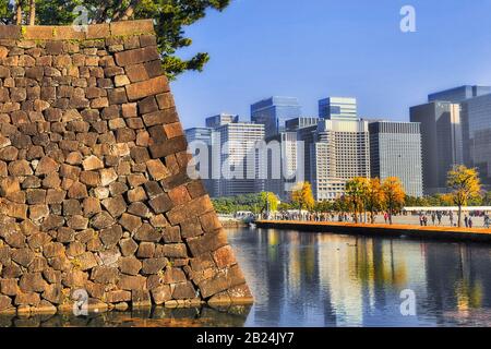 Water moat around strong stone walls of a park and gardens in Tokyo CBD on a sunny day with crowds of tourists. Stock Photo