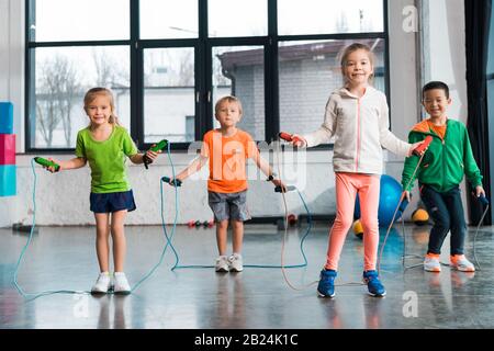 Front view of multiethnic children doing exercise with jump rope in gym Stock Photo