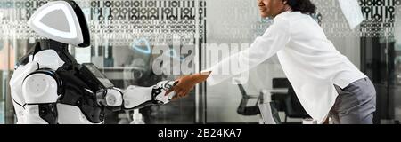panoramic shot of african american businesswoman shaking hands with robot in office Stock Photo