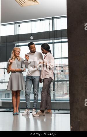 young multicultural businesspeople having discussion while standing in office and looking at documents Stock Photo
