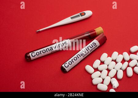 Pills, thermometer and test tubes with blood samples and coronavirus lettering on red surface Stock Photo