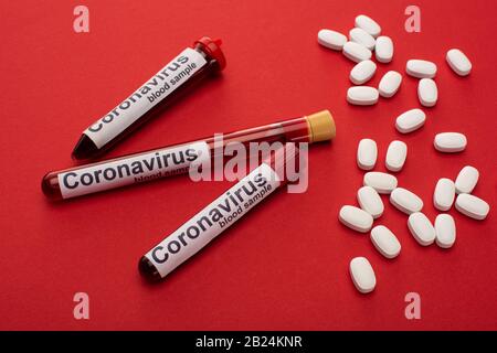 Close up view of pills and test tubes with blood samples and coronavirus lettering on red background Stock Photo