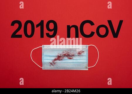 Top view of 2019 ncov lettering with blood on medical mask isolated on red Stock Photo