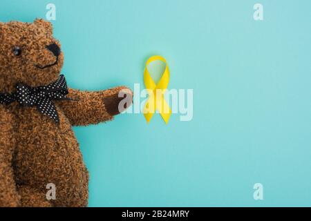 Top view of teddy bear with bow and yellow ribbon on blue background, international childhood cancer day concept Stock Photo