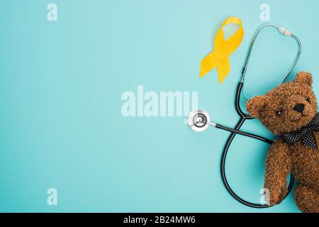 Top view of yellow ribbon, toy and stethoscope on blue background, international childhood cancer day concept Stock Photo