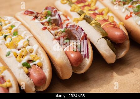 various delicious hot dogs with vegetables and sauces on wooden table Stock Photo