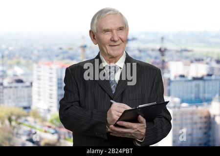 Old man in suit writing down on clipboard. Stock Photo