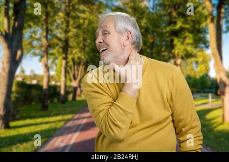 Old grandpa having neckache in the park. Stock Photo