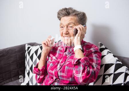 Theme old person uses technology. Mature happy joy smile active gray hair Caucasian wrinkles woman sitting home in living room on the sofa and using a Stock Photo